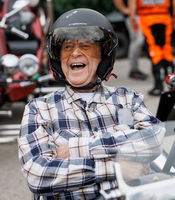 Älterer Mann mit Helm lacht fröhlich in einem Fahrzeug.