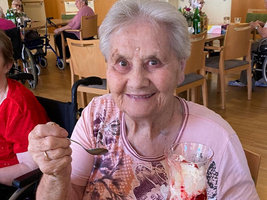 Eine lächelnde ältere Frau hält ein Dessertglas mit Eis und Früchten.