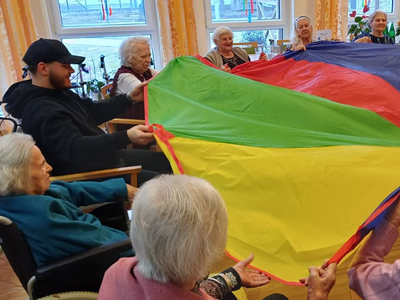 Senioren und ein Betreuer spielen gemeinsam mit einem bunten Spieltuch.