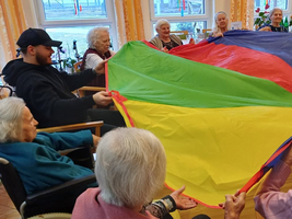 Senioren und ein Betreuer spielen gemeinsam mit einem bunten Spieltuch.