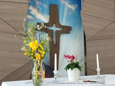 Ein Tisch mit Blumen, Kerzen und einem Kreuz im Hintergrund.
