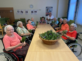 Ältere Frauen sitzen an einem Tisch mit Frischblumen und Kräutern in Händen.
