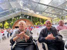Zwei ältere Menschen im Vordergrund applaudieren, Publikum sitzt in Stühlen dahinter.