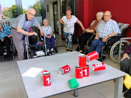 Ältere Menschen spielen ein Spiel mit roten Dosen und bunten Würfeln.