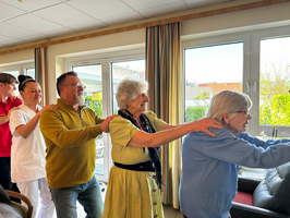 Eine Gruppe von Personen macht eine Kettenbewegung in einem hellen Raum.