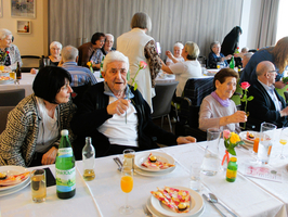 Ältere Menschen feiern gemeinsam bei einem Essen und halten Rosen in der Hand.