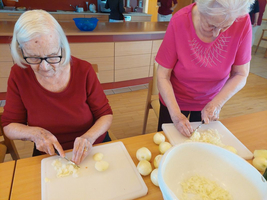 Zwei ältere Frauen schneiden Zwiebeln und Kartoffeln in einer gemütlichen Küche.