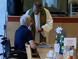 Ein Pastor reicht einer älteren Person in einem Rollstuhl den Kommunionkelch.