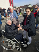 Zwei Frauen, eine im Rollstuhl, halten sich an den Händen und lächeln.