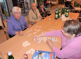 Ältere Frauen spielen ein Gesellschaftsspiel mit Spielsteinen an einem Tisch.