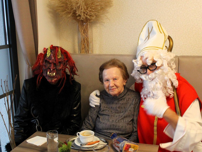 Frau sitzt zwischen zwei verkleideten Personen, einer als Nikolaus, der andere als Teufel.