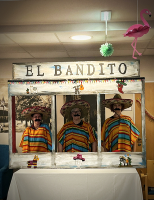 Drei Personen in bunten Ponchos und Sombreros stehen hinter einem Fotoautomat.