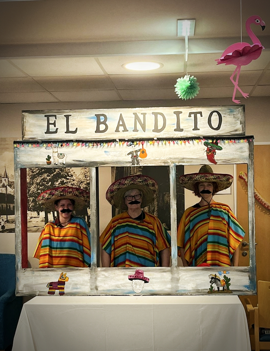 Drei Personen in bunten Ponchos und Sombreros stehen hinter einem Fotoautomat.