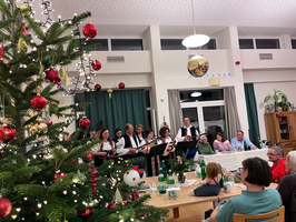 Weihnachtsfeier mit Gesang und einer festlich geschmückten Tanne im Vordergrund.