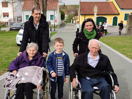 Familie begleitet Senioren im Rollstuhl auf einem Spaziergang im Freien.