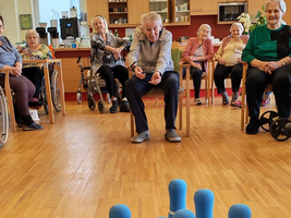 Ältere Menschen spielen Bowling mit blauen Kegel in einem Gemeinschaftsraum.