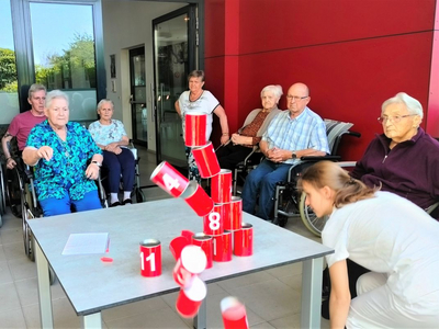 Senioren beobachten eine Spielaktivität mit roten Dosen auf einem Tisch.