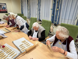 Ältere Menschen backen gemeinsam Kekse in einem Raum mit Tischen und Stühlen.