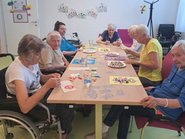 Ältere Frauen arbeiten gemeinsam an Bastelprojekten an einem Tisch.