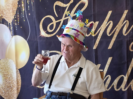Ein älterer Mann mit Hut feiert seinen Geburtstag und hält ein Getränk.