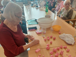 Seniorinnen gestalten rosa Figuren aus Modelliermasse an einem Tisch.