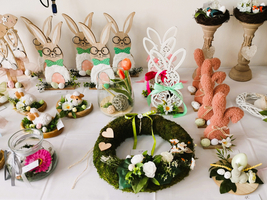 Osterdekorationen mit Hasen, Blumen und einem Mooskranz auf einem Tisch arrangiert.