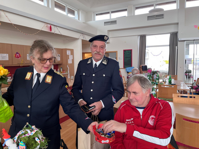 Drei Personen, darunter ein Mann im Polizeiuniform, stehen in einem festlich geschmückten Raum.