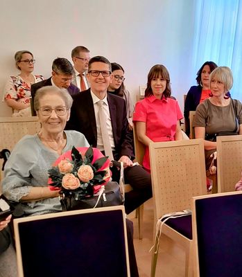 Eine Frau im Rollstuhl hält Blumen und sitzt in einer Menschenmenge.