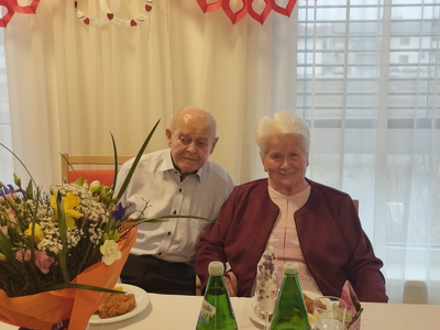 Ein älteres Paar sitzt an einem Tisch mit Blumenstrauß.