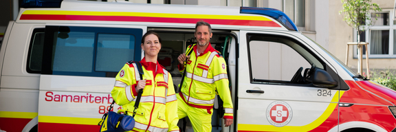 Mitarbeiter:innen im Rettungsdienst vor Rettungsauto