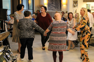 Fünf Frauen tanzen fröhlich in einem Saal voller Menschen.