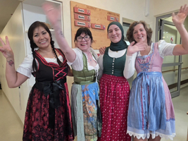 Vier Frauen in traditionellen Trachten posieren fröhlich und winken.
