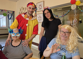 Ein Clown und drei Personen feiern fröhlich in einem Seniorenheim.