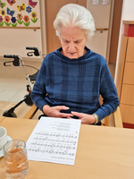 Eine ältere Frau sitzt am Tisch und liest Notenblätter.