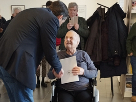 Ein älterer Mann sitzt im Rollstuhl und erhält ein Dokument von einem Gesprächspartner.
