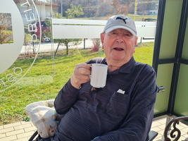 Ein älterer Mann in einem Rollstuhl hält eine Tasse Kaffee in der Hand.