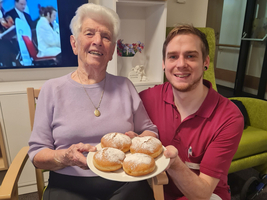 Ältere Frau und junger Mann halten eine Platte mit Berliner-Pfannkuchen.