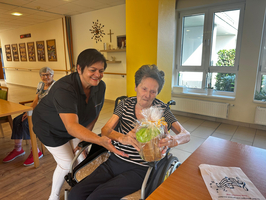 Eine Frau überreicht einer älteren Dame ein Geschenk in einem Gemeinschaftsraum.