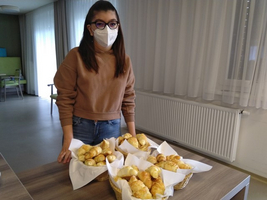 Eine Person trägt eine Maske und steht vor Körben mit frischem Gebäck.