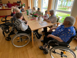 Ältere Menschen in Rollstühlen sitzen an einem Tisch und unterhalten sich.