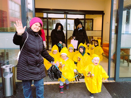 Eine Frau und Kinder in Regencapes gehen nach draußen.