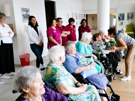 Feierliche Begegnung mit Blumen zwischen Pflegepersonal und Seniorinnen.