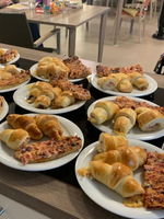 Mehrere Teller mit Croissants und Pizzastückchen auf einem Tisch.