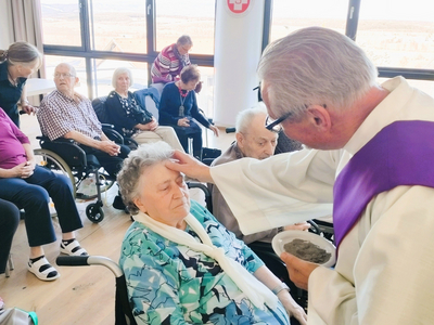 Ein Priester segnet eine ältere Frau in einer Gruppe von Senioren.