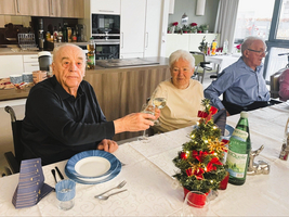 Ältere Menschen stoßen mit Gläsern an, dekorierter Tisch mit Weihnachtsbaum.
