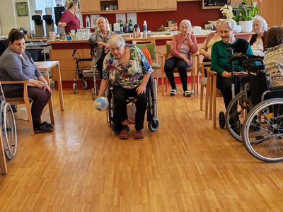 Eine Gruppe älterer Menschen spielt mit blauen Bowlingkegeln in einem Gemeinschaftsraum.