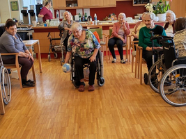 Eine Gruppe älterer Menschen spielt mit blauen Bowlingkegeln in einem Gemeinschaftsraum.