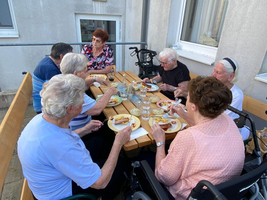Eine Gruppe älterer Menschen sitzt bei einem Essen an einem Tisch im Freien.