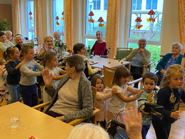 Kinder tanzen und singen mit älteren Menschen in einem Gemeinschaftsraum.