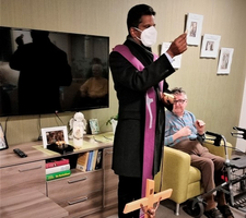 Ein Priester segnet mit einem Kreuz in einem Wohnraum.